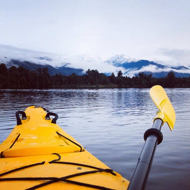 View from a kayak across a still lake towards snow-capped New Zealand mountains